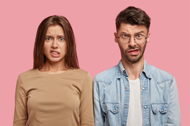 Foto gratuita pareja joven desconcertado posando contra la pared rosa