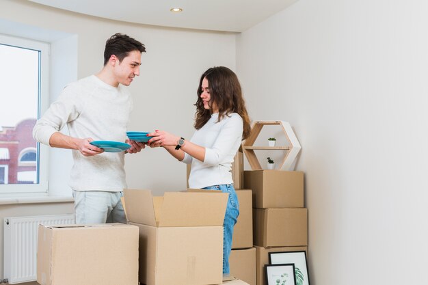 Pareja joven desempacando los platos azules de cajas de cartón en su nueva casa