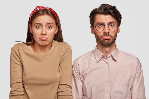 Pareja joven despistada posando contra la pared blanca