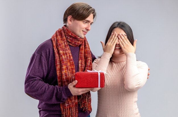 Pareja joven en el día de San Valentín chico complacido dando caja de regalo a chica aislada sobre fondo blanco.