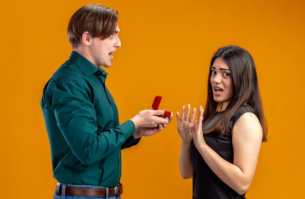 Pareja joven en el día de San Valentín chico enojado dando anillo de bodas a una chica descontenta aislada sobre fondo naranja