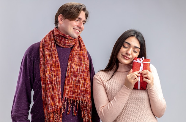 Pareja joven en el día de San Valentín chico sonriente mirando a niña complacida con caja de regalo aislado sobre fondo blanco.