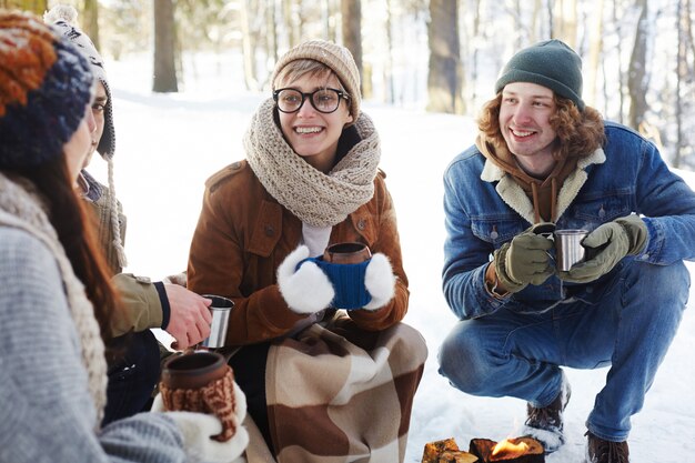 Pareja joven disfrutando de bebidas en el bosque de invierno