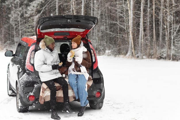 Pareja joven disfrutando de bebidas calientes y un sándwich durante un viaje por carretera de invierno