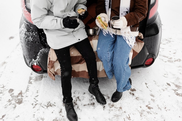 Pareja joven disfrutando de bebidas calientes y un sándwich durante un viaje por carretera de invierno