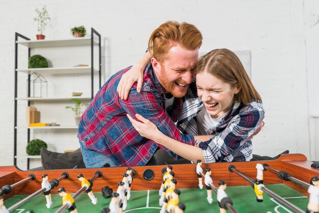 Pareja joven disfrutando detrás de la mesa de fútbol en casa