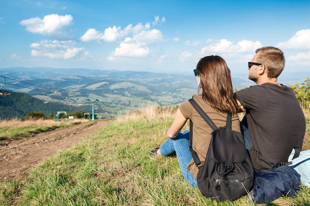 Pareja joven disfrutando del paisaje de montañas, sentado en la colina