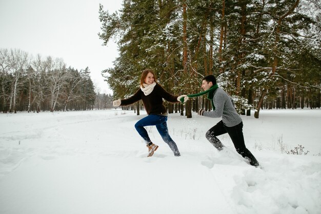 Pareja joven divirtiéndose en el bosque de pinos nevados. Invierno.