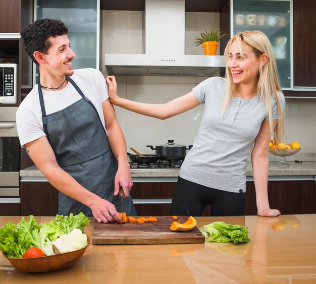 Pareja joven divirtiéndose mientras corta verduras en la cocina