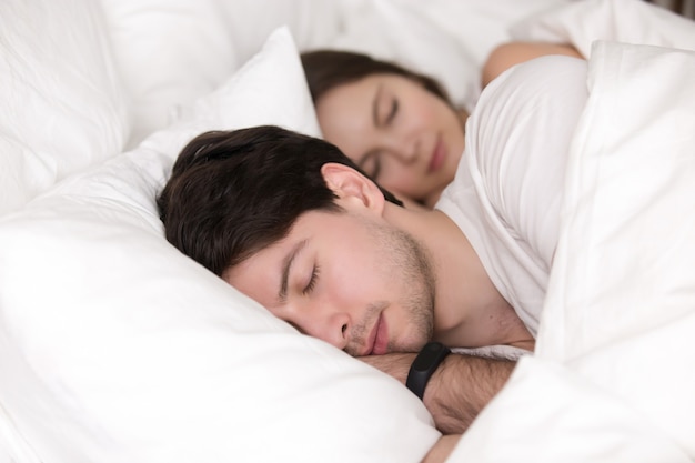 Pareja joven durmiendo en la cama, hombre con rastreador de reloj inteligente