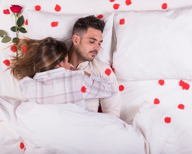 Pareja joven durmiendo en la cama con pétalos de rosa.