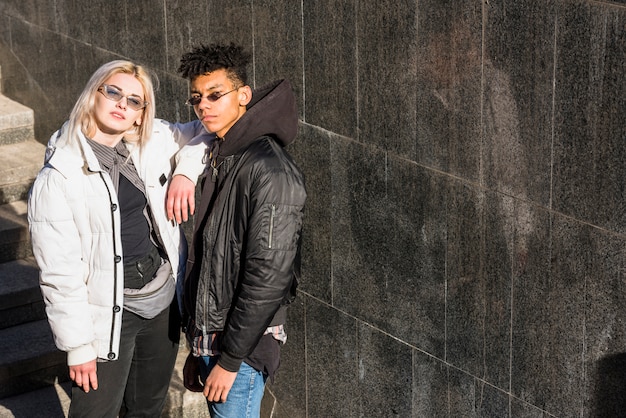 Foto gratuita pareja joven elegante con gafas de sol de pie al aire libre