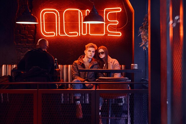 Pareja joven elegante vestida de moda sentada en un café con interior industrial