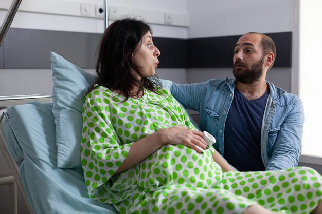 Pareja joven con embarazo sentada en la cama de la sala de hospital