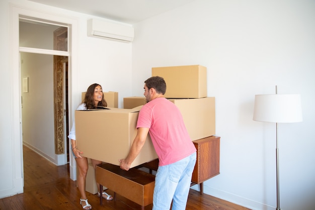 Pareja joven emocionada mudarse a un piso nuevo, llevando cajas de cartón con cuidado