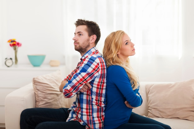 Foto gratuita pareja joven enojado sentados espalda con espalda en casa