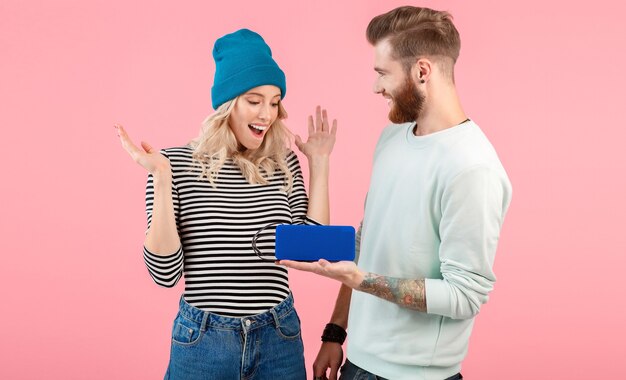 Pareja joven escuchando música en un altavoz inalámbrico vistiendo un traje elegante y fresco sonriendo posando en rosa