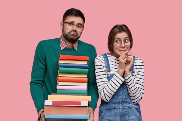 Pareja joven de estudiantes se para cerca, sostienen la pila de libros, estudian juntos, se preparan para el seminario