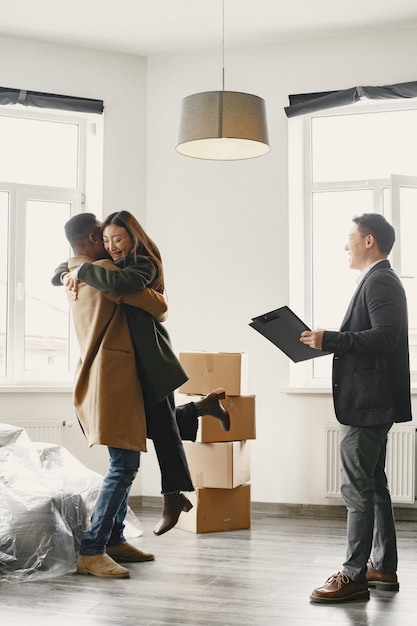 Pareja joven exitosa convertirse en propietarios. Chica salta al abrazo de los brazos de su novio. Casa espaciosa y luminosa con grandes ventanales.