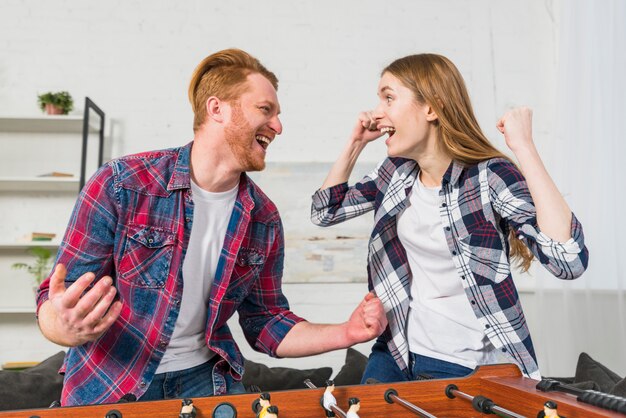 Pareja joven exitosa disfrutando el juego de futbol de mesa en casa