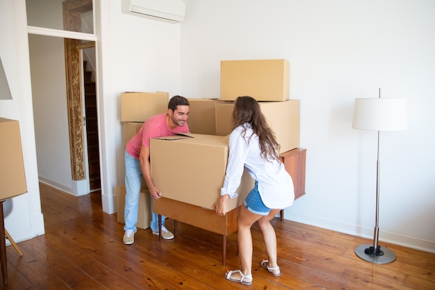 Pareja joven de la familia mudándose a un nuevo apartamento, llevando cajas de cartón y muebles