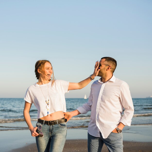 Pareja joven feliz burlando en la playa contra el cielo azul