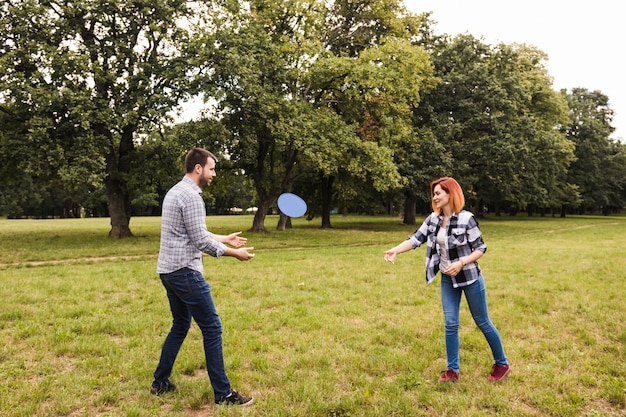 Pareja joven feliz jugando con disco volador en el jardín