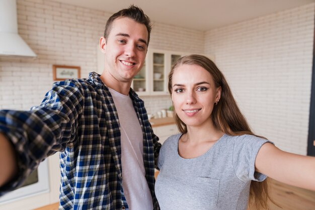 Pareja joven feliz juntos haciendo selfie en cocina