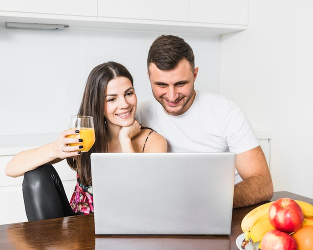 Pareja joven feliz mirando portátil en la cocina