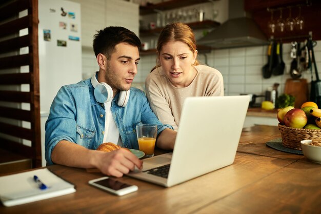 Pareja joven hablando mientras usa la computadora portátil en casa