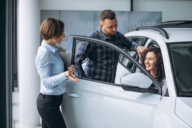 Pareja joven hablando con un vendedor en una sala de exposición de automóviles