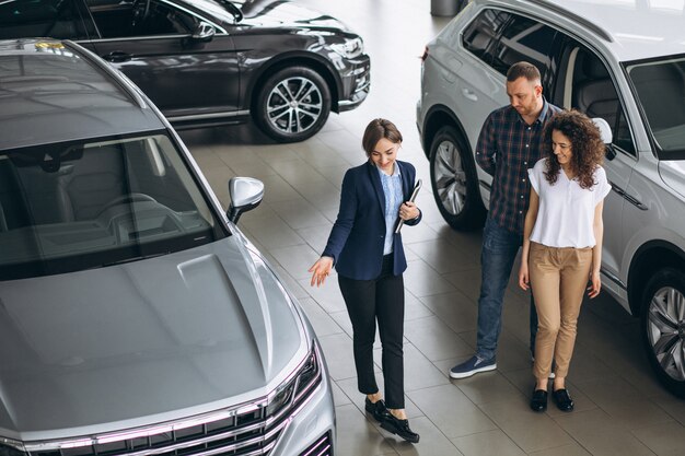 Pareja joven hablando con un vendedor en una sala de exposición de automóviles