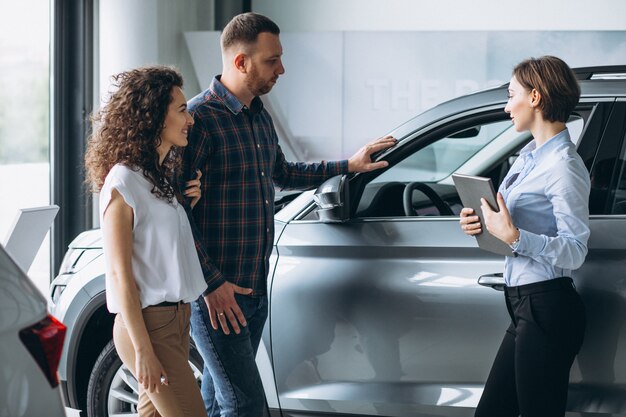 Pareja joven hablando con un vendedor en una sala de exposición de automóviles