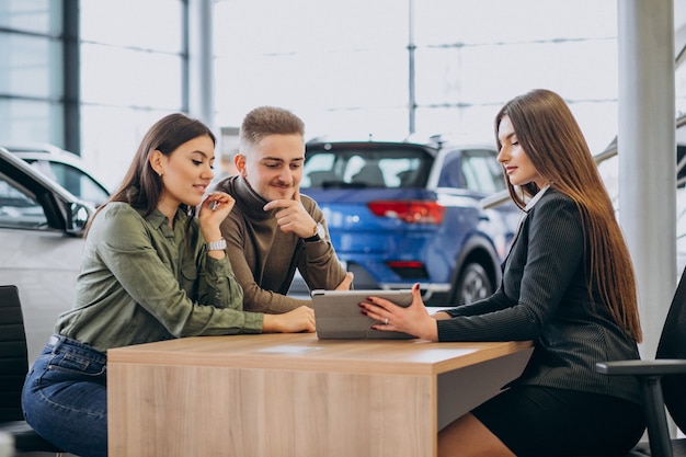 Pareja joven hablando con un vendedor en una sala de exposición de automóviles