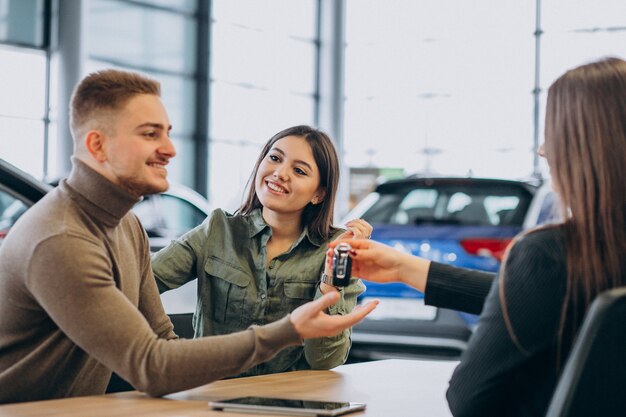 Pareja joven hablando con un vendedor en una sala de exposición de automóviles