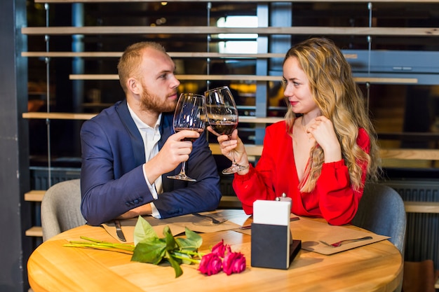 Pareja joven haciendo copas de vino en la mesa en el restaurante