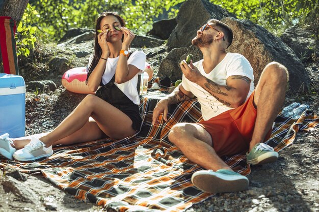 Pareja joven haciendo un picnic en la orilla del río en un día soleado.