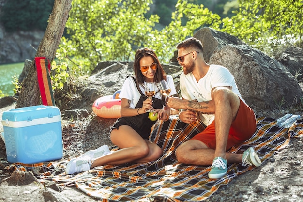 Pareja joven haciendo un picnic en la orilla del río en un día soleado.