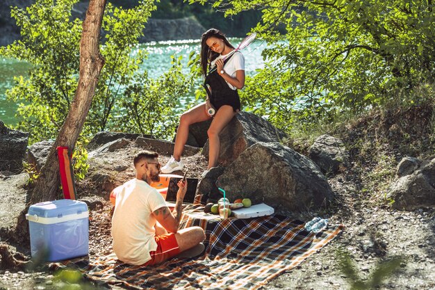Pareja joven haciendo un picnic en la orilla del río en un día soleado