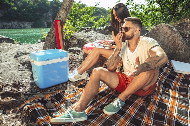 Pareja joven haciendo un picnic en la orilla del río en un día soleado