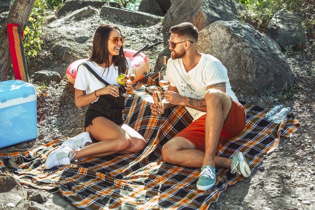 Pareja joven haciendo un picnic en la orilla del río en un día soleado