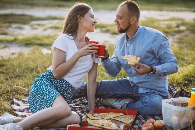 Pareja joven haciendo un picnic con pizza en el parque