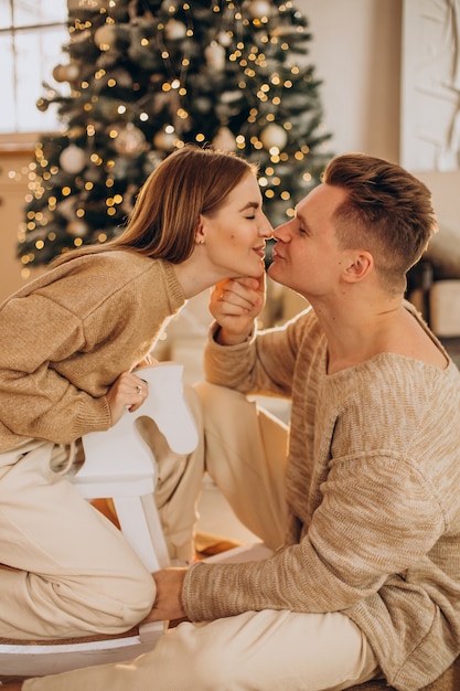 Pareja joven haciendo regalos el uno al otro por el árbol de navidad