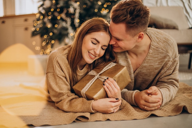 Pareja joven haciendo regalos el uno al otro por el árbol de navidad