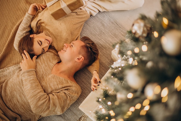 Pareja joven haciendo regalos el uno al otro por el árbol de navidad