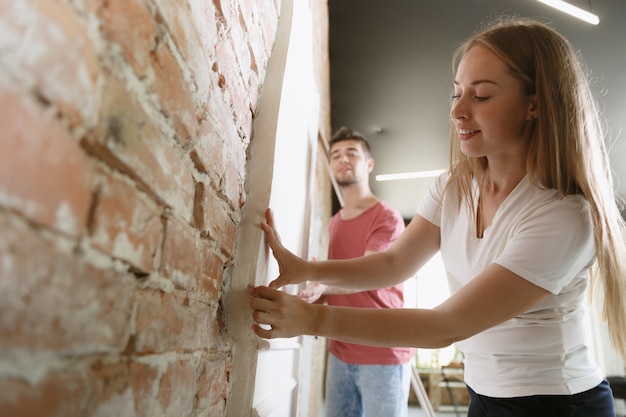 Pareja joven haciendo reparación de apartamentos juntos ellos mismos. Hombre y mujer casados haciendo remodelación o renovación de la casa. Concepto de relaciones, familia, amor. Midiendo la pared, preparándose para el diseño.