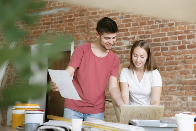 Pareja joven haciendo reparación de apartamentos juntos ellos mismos. Hombre y mujer casados haciendo remodelación o renovación de la casa