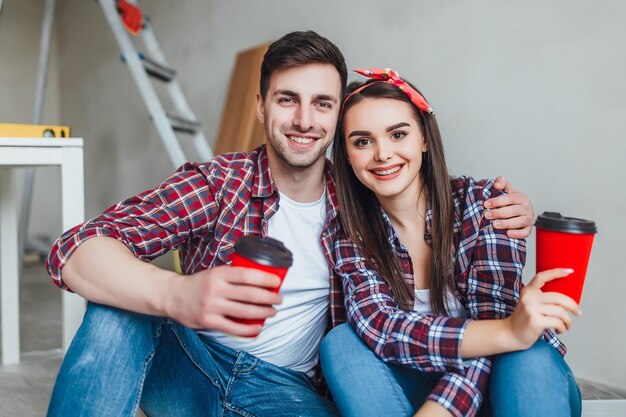 Pareja joven haciendo reparaciones, tenga un descanso con una taza de café sabroso. Se abrazan en casa nueva