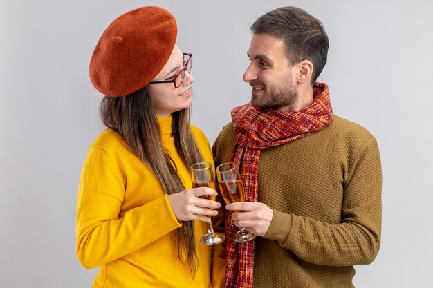 Pareja joven hermosa feliz hombre y mujer sonriente en boina con vasos de champán sonriendo alegremente feliz en el amor juntos celebrando el día de San Valentín de pie sobre una pared blanca