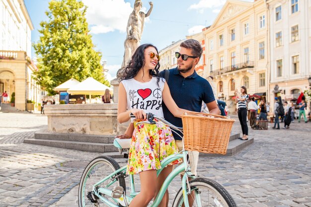 Pareja joven hermosa hipster enamorada caminando con bicicleta en la calle de la ciudad vieja